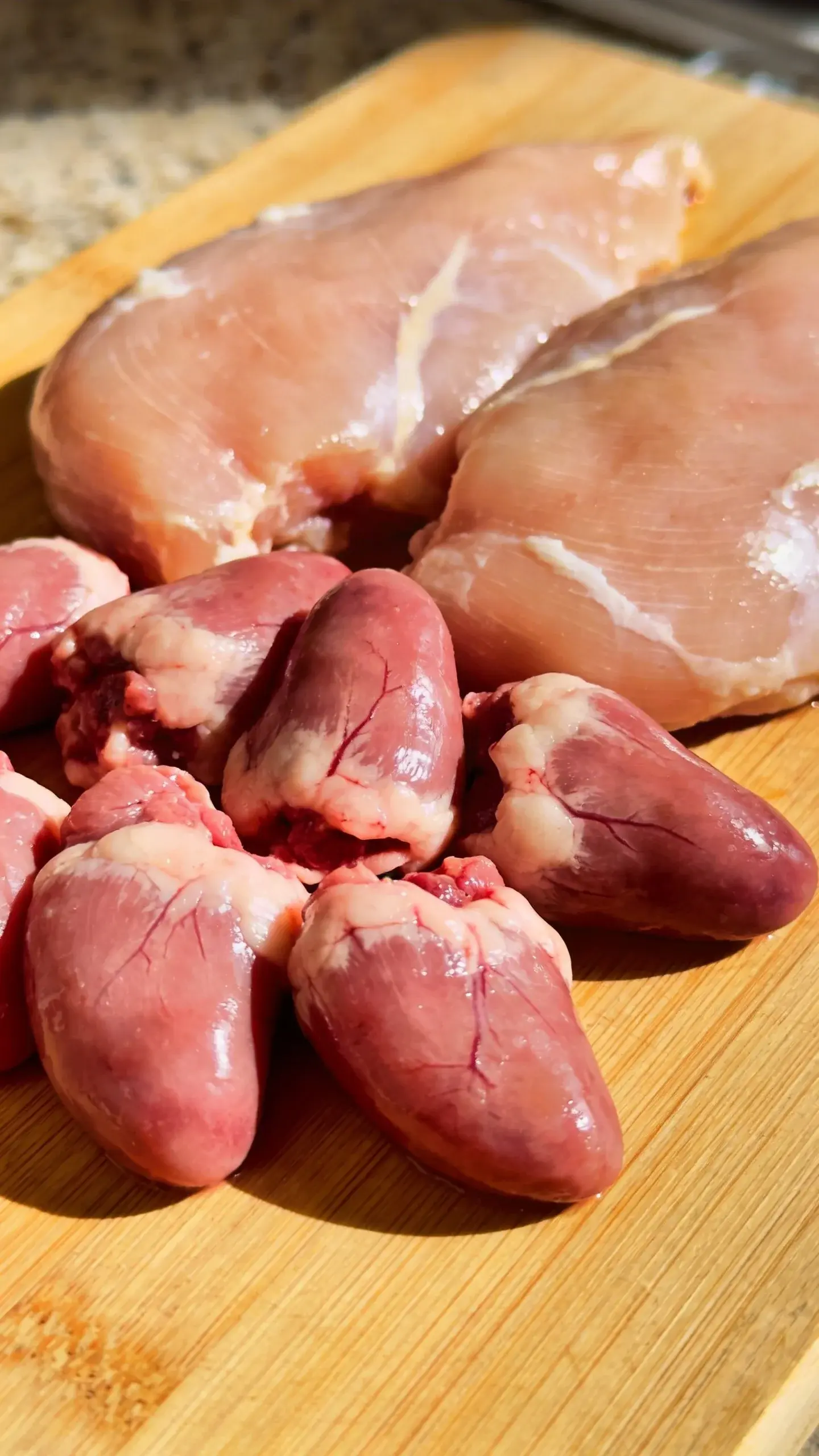 raw chicken hearts and thighs on cutting board, taurine focus